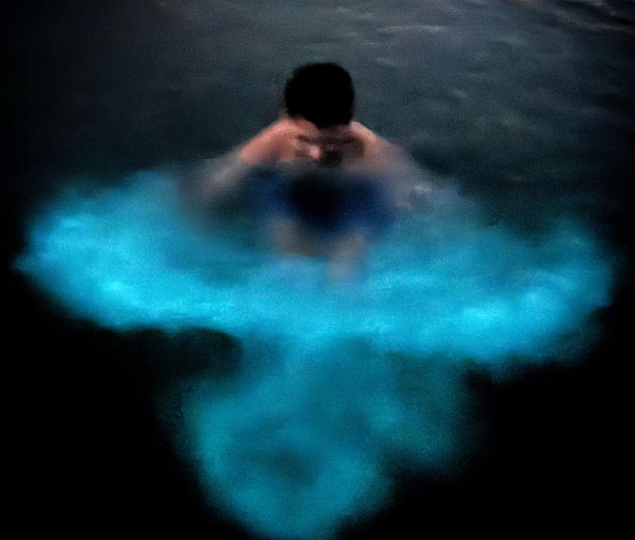 A guest swimming in the glowing water of the bioluminescent bay
