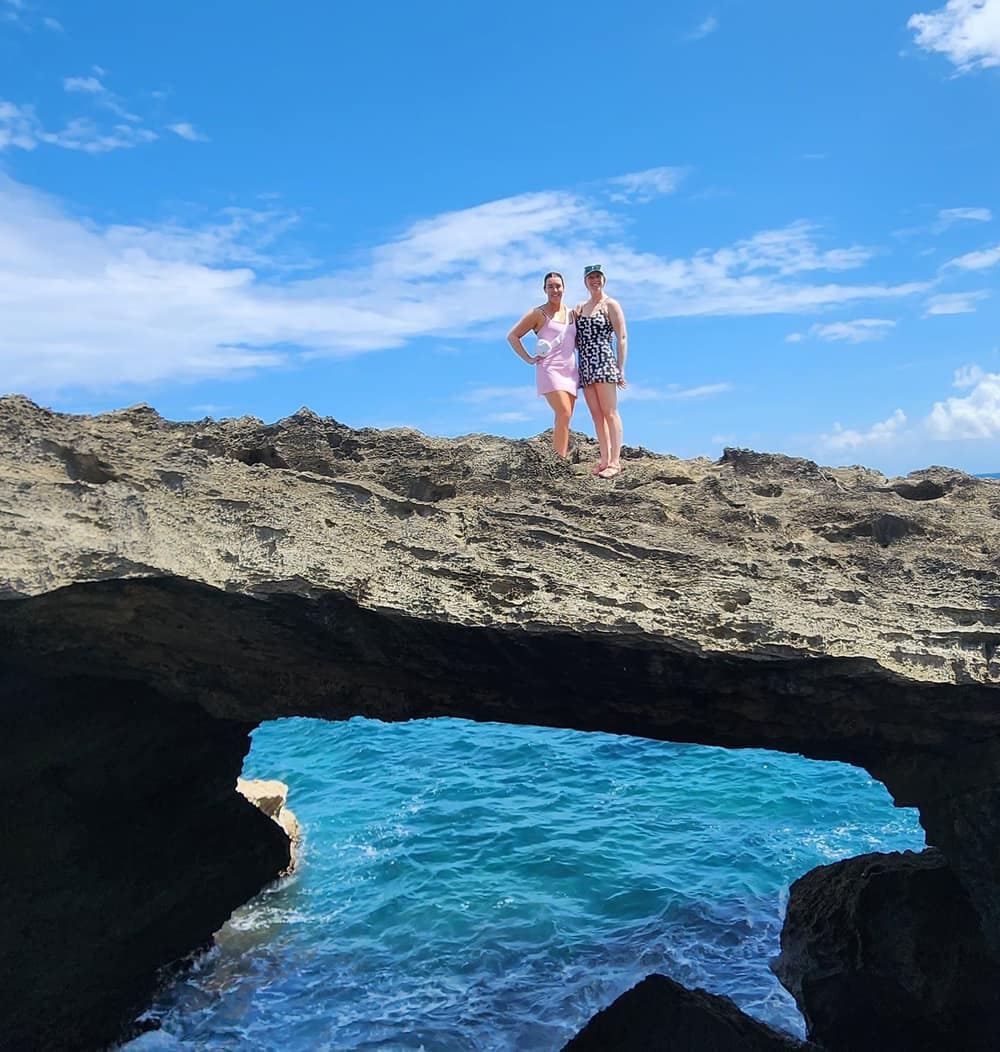 Two guests standing on a natural sea arch on the north coast